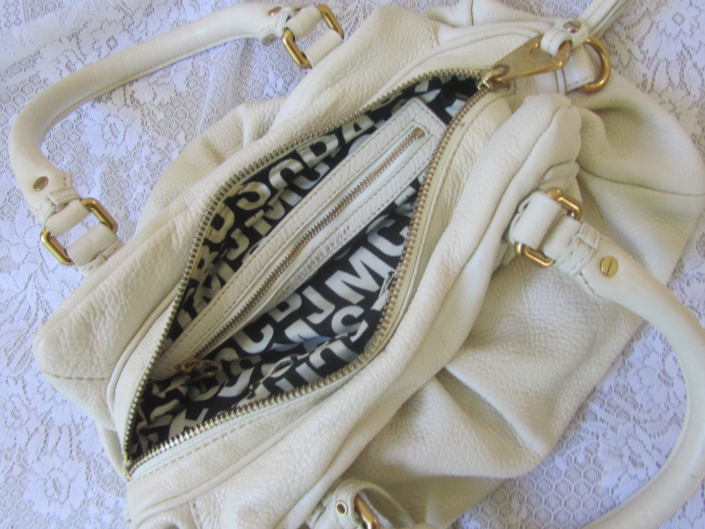 Cream-colored handbag with gold accents on a textured white background