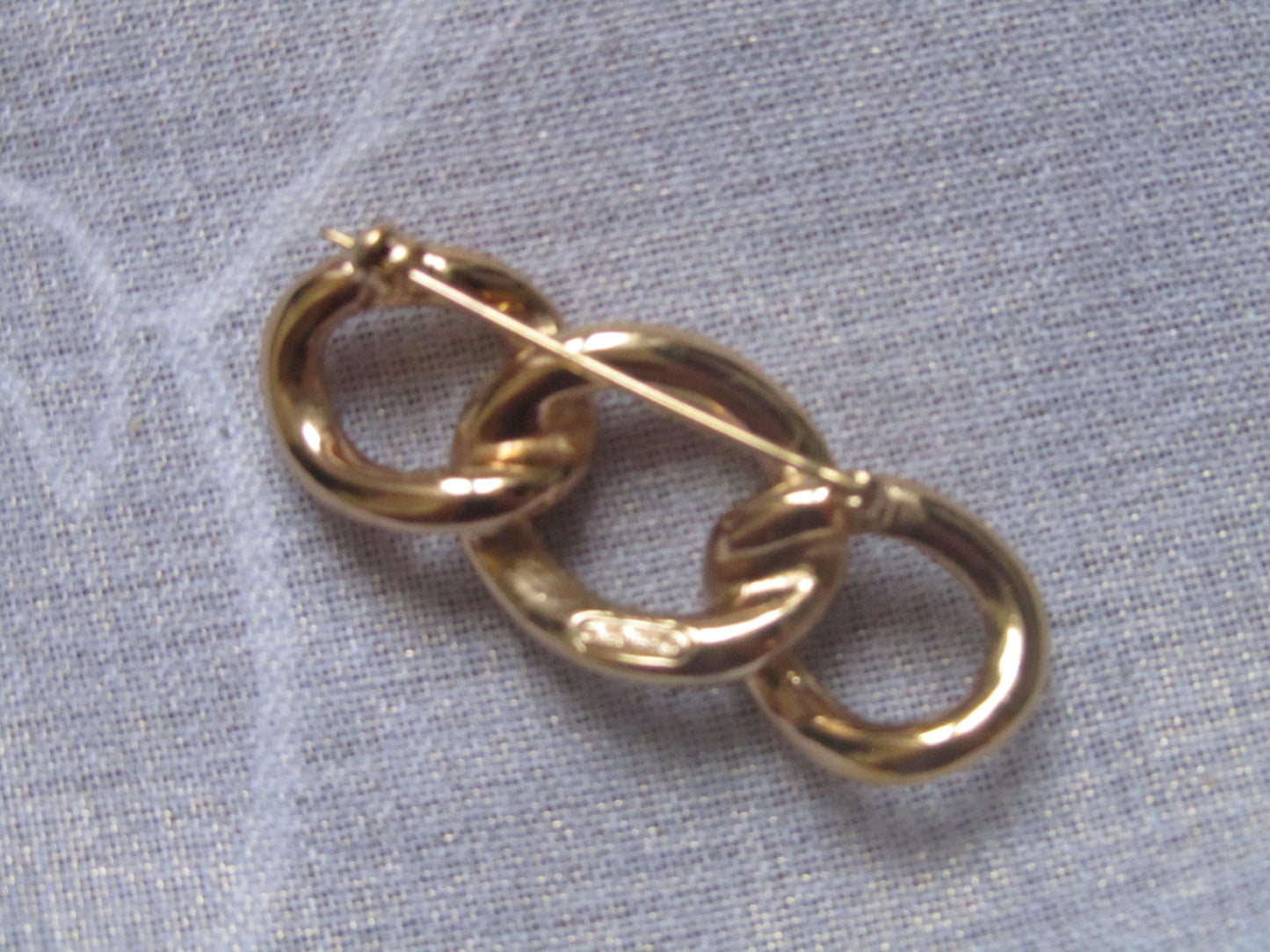 Gold and silver interlocking brooch on a light gray fabric background