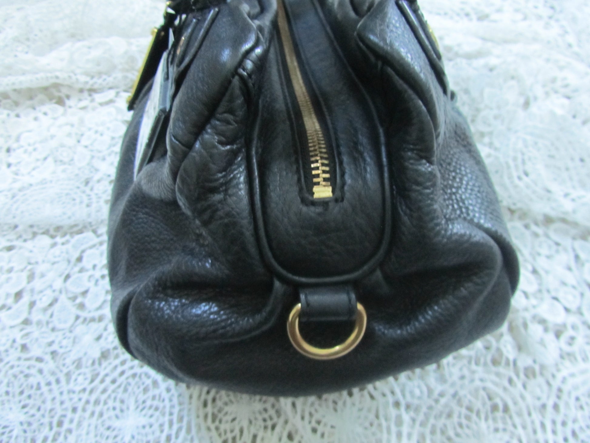 Black leather handbag with gold zipper and ring on a textured white surface