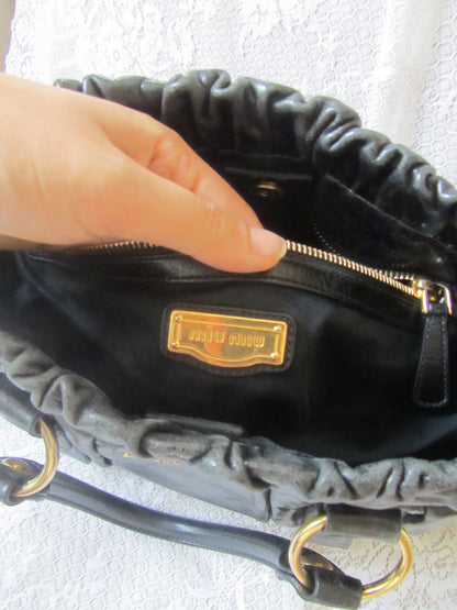 Black handbag with gold zipper and visible brand logo on a light gray background