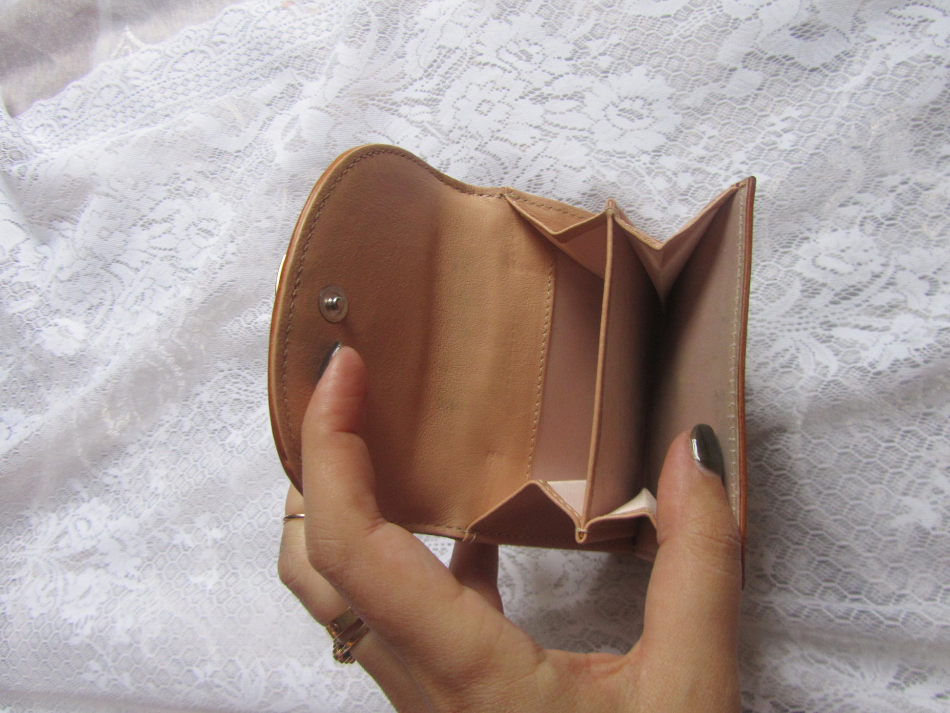 Hand holding an open tan leather wallet against a textured white background