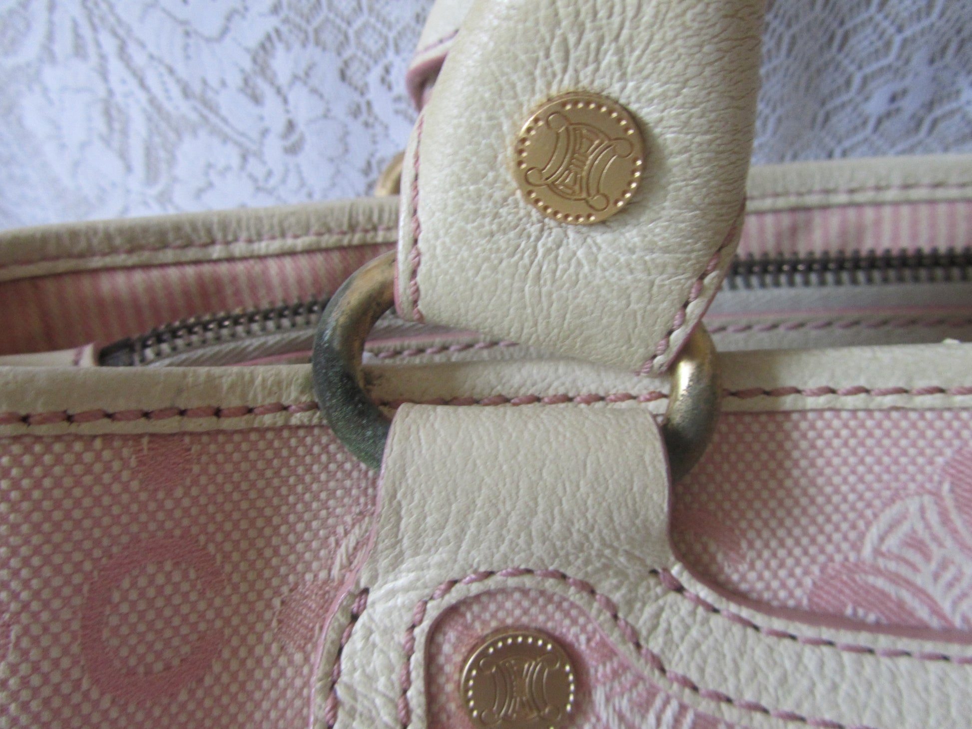 Close-up of a pink handbag with gold hardware against a lace curtain background