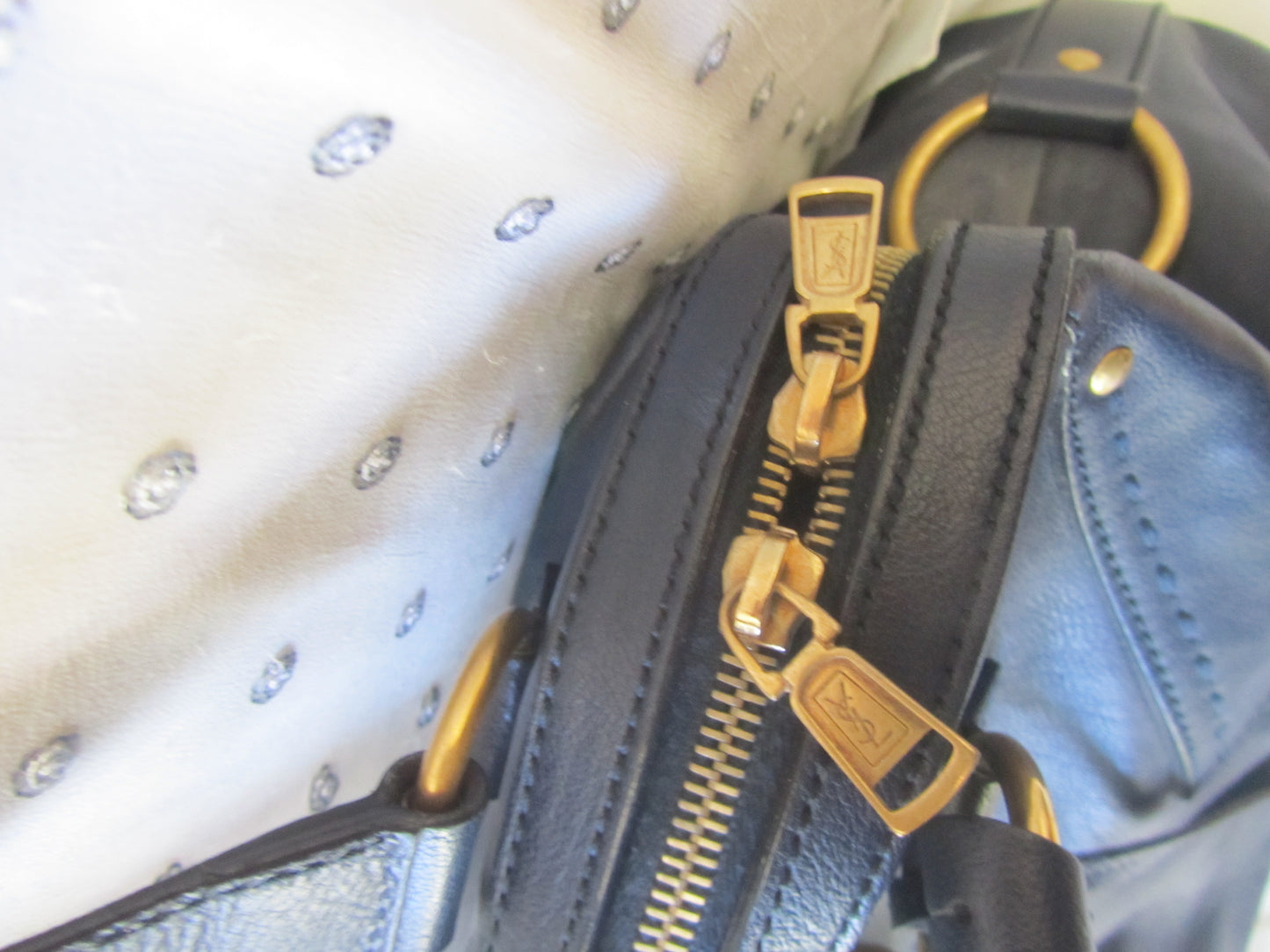 Close-up of a gold zipper on a black leather bag with a white interior.