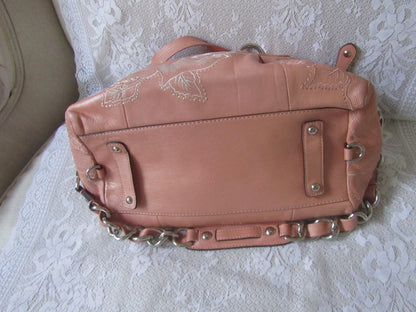 Pink leather handbag with chain detail on a textured surface