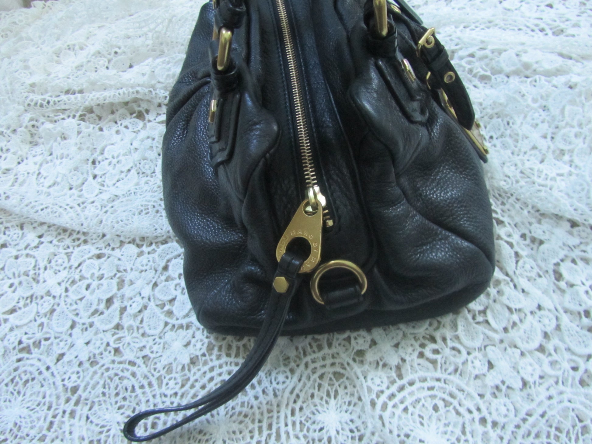 Black leather handbag with gold zipper on a white lace background
