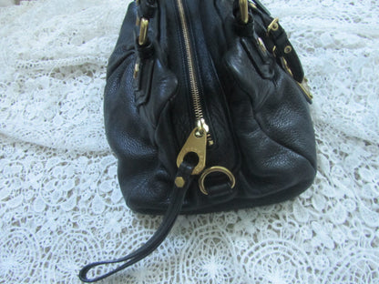 Black leather handbag with gold zipper on a white lace background