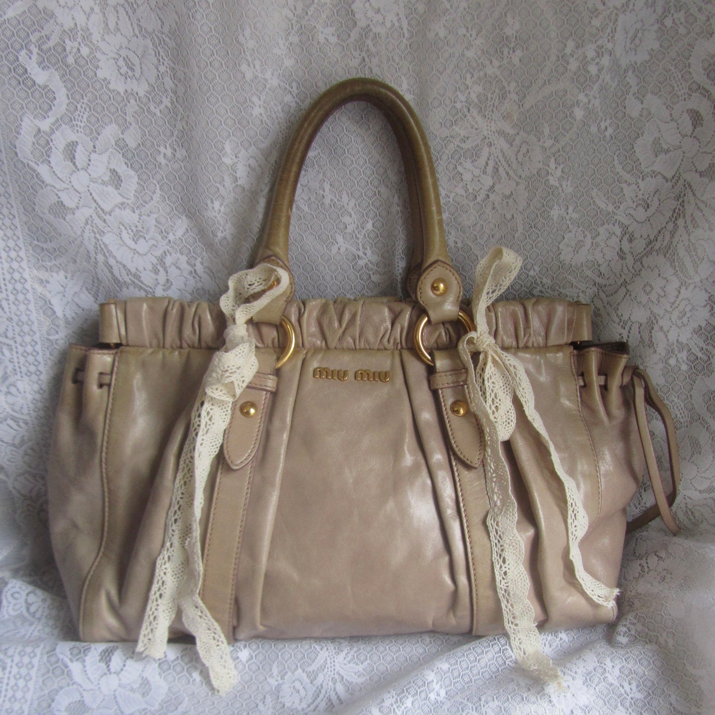 miu miu vintage beige handbag with lace ribbons on a white textured surface