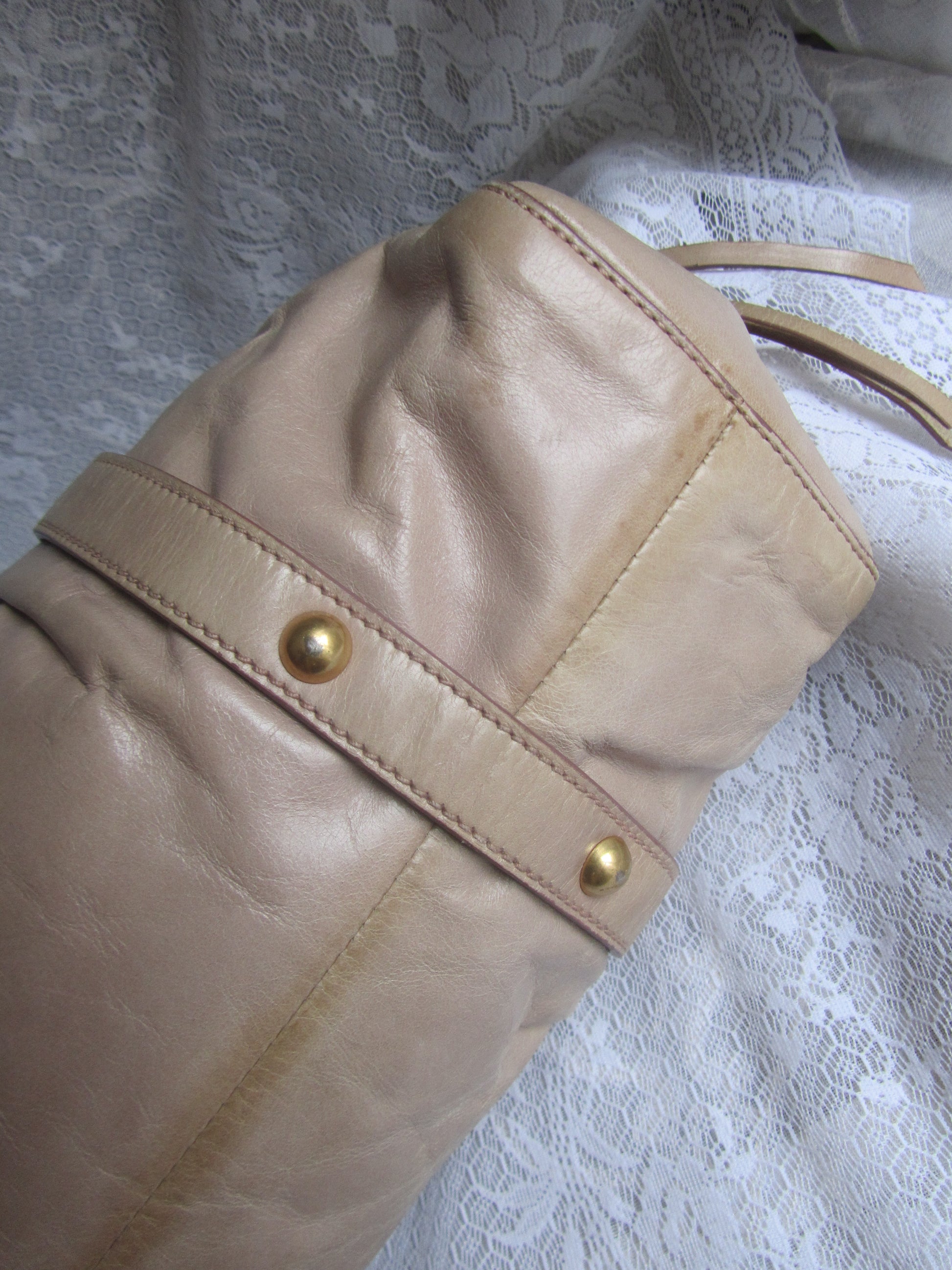 Close-up of a beige leather bag with gold studs on a textured white background