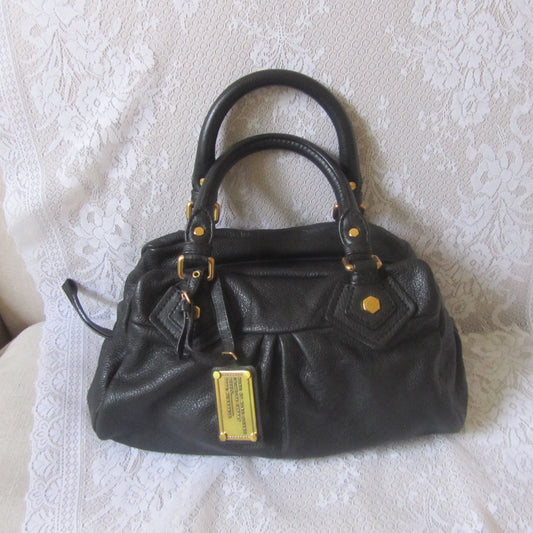 Black handbag with gold accents on a textured white surface