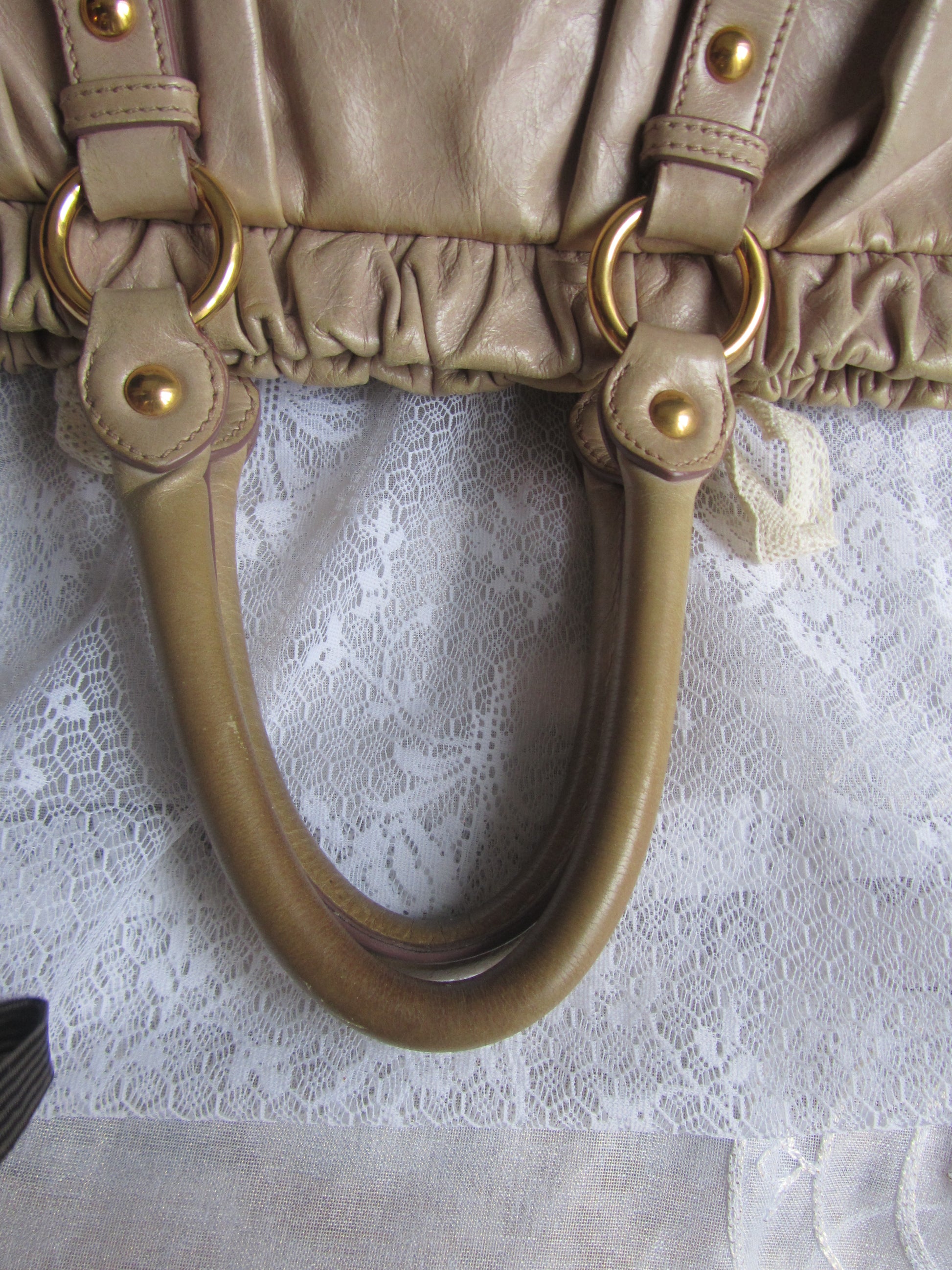 Close-up of a beige handbag handle with gold hardware on a textured white background
