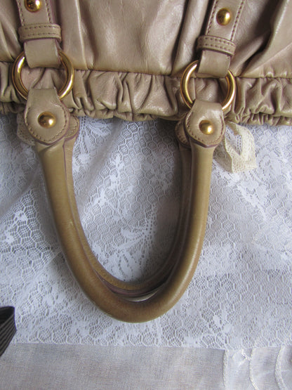 Close-up of a beige handbag handle with gold hardware on a textured white background