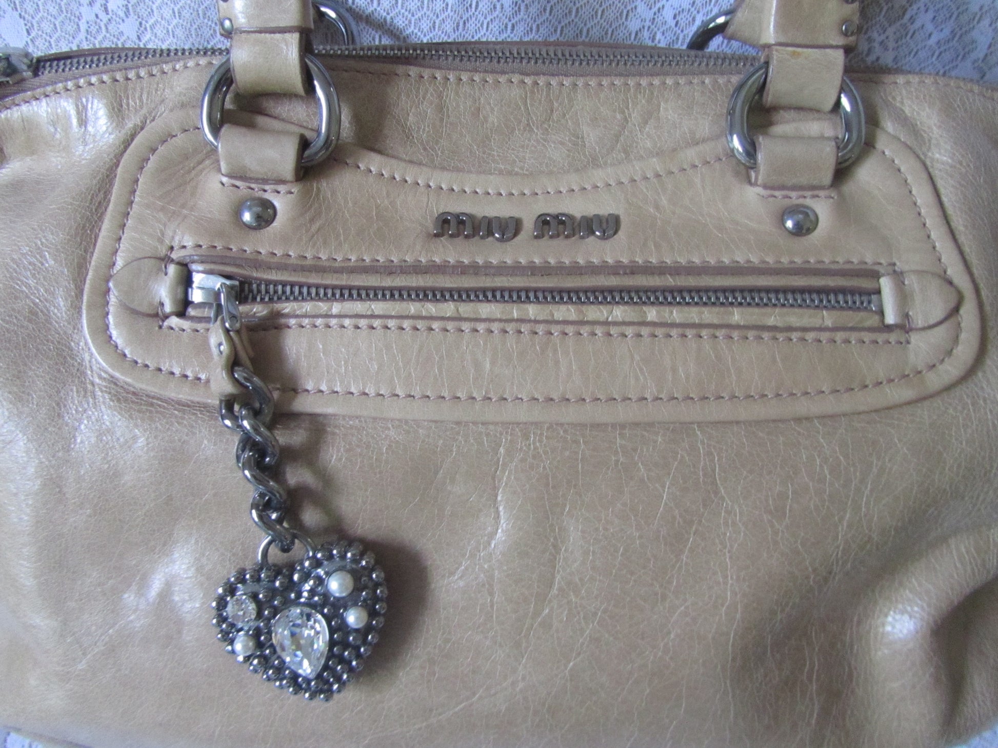 Beige handbag with a heart-shaped charm on a textured surface