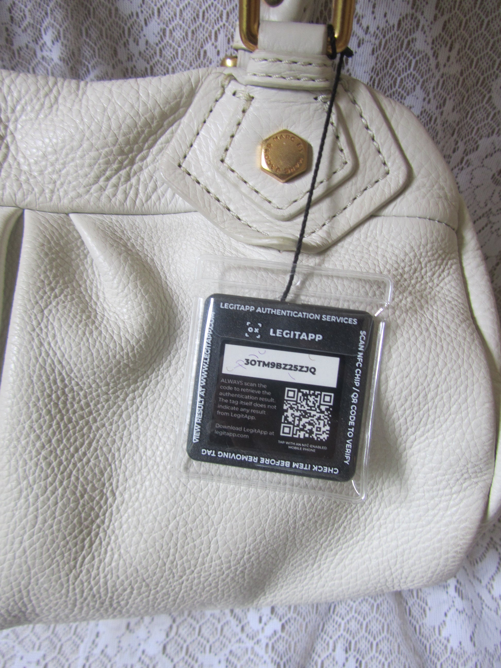 Close-up of a beige leather handbag with a visible brand label on a textured surface.