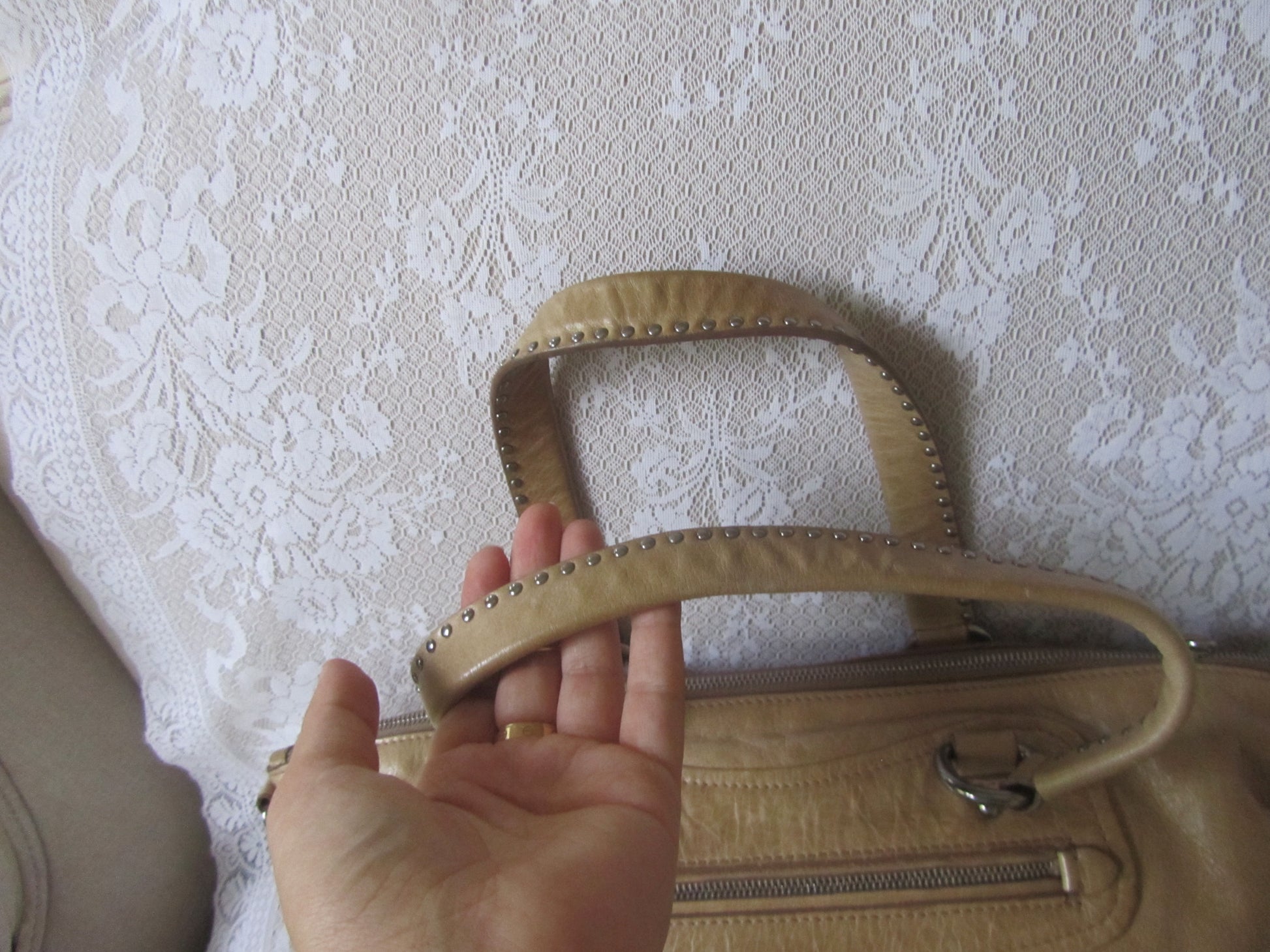 Beige handbag held by a hand against a textured white background