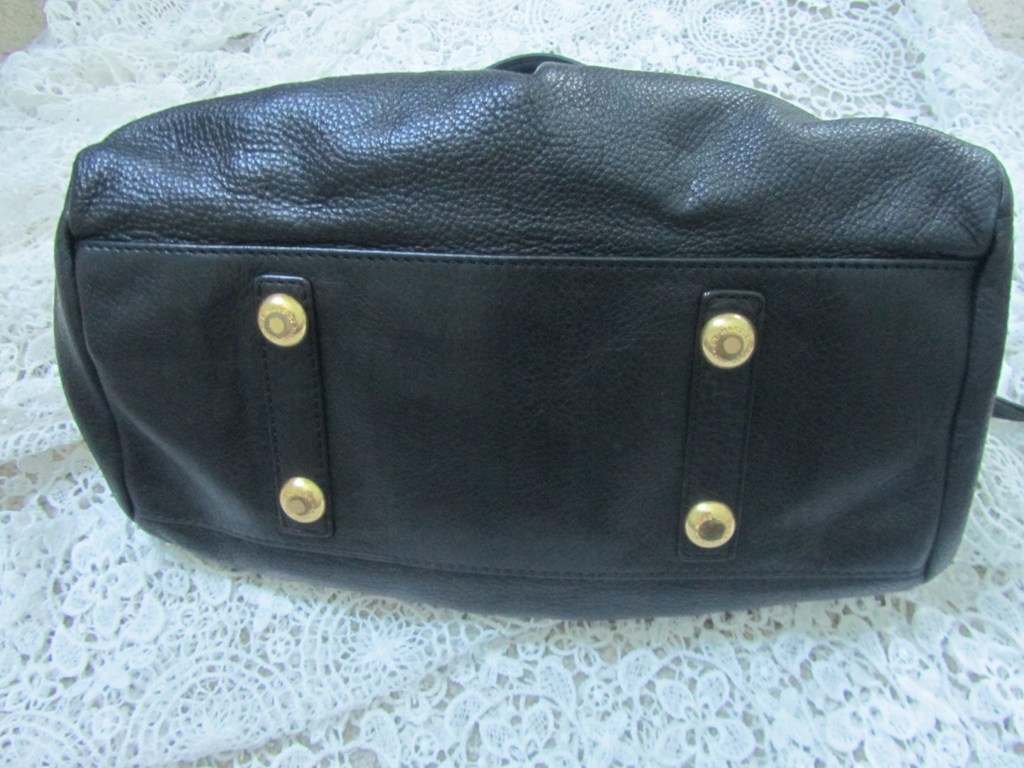 Black leather bag with gold studs on a textured white surface