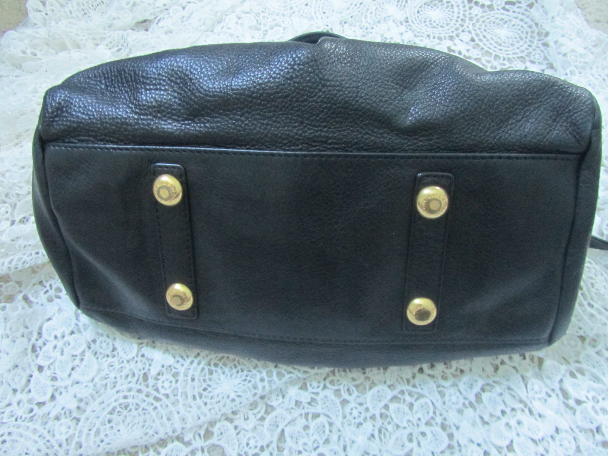 Black leather bag with gold studs on a textured white surface
