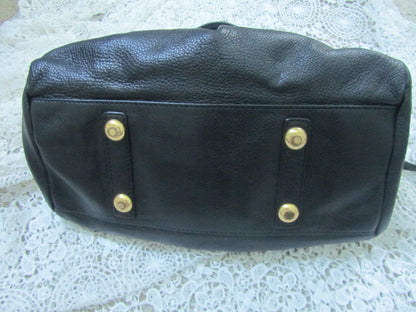 Black leather bag with gold studs on a textured white surface