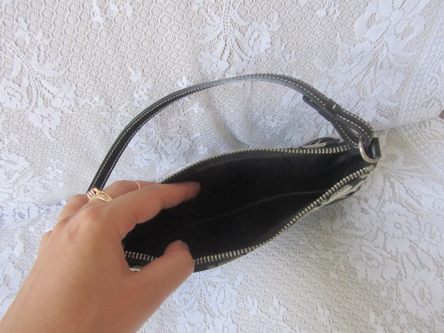 Hand opening a black clutch bag on a textured white background