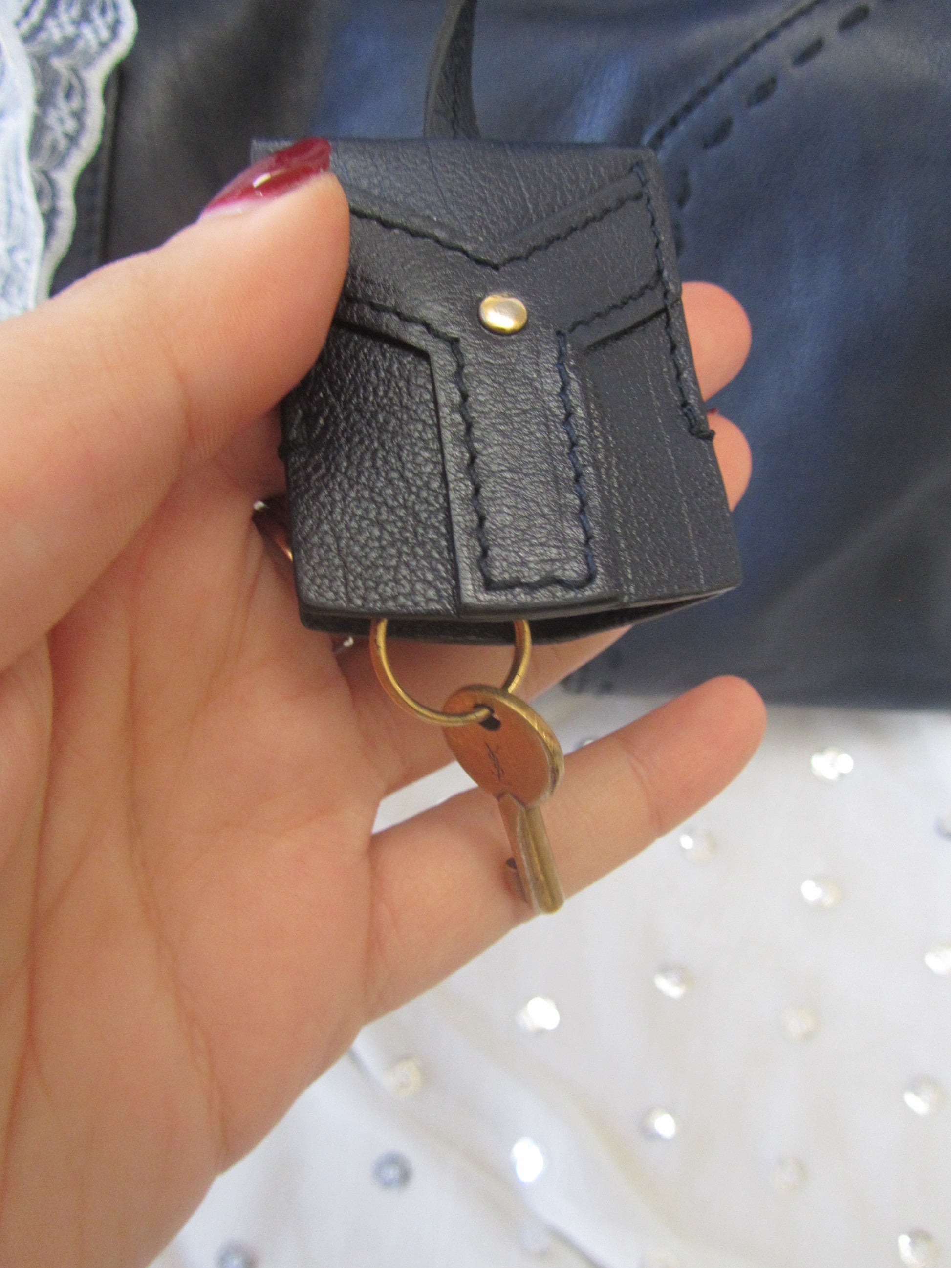Black leather key case with gold ring held in a hand against a blurred background