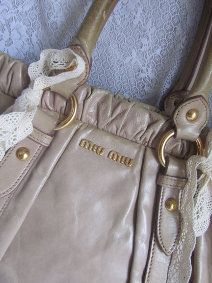 Close-up of a beige handbag with gold hardware on a lace background