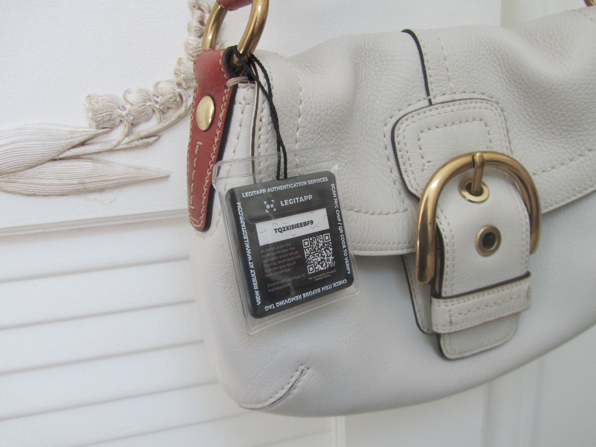 White handbag with a gold buckle and a visible authenticity tag on a white background