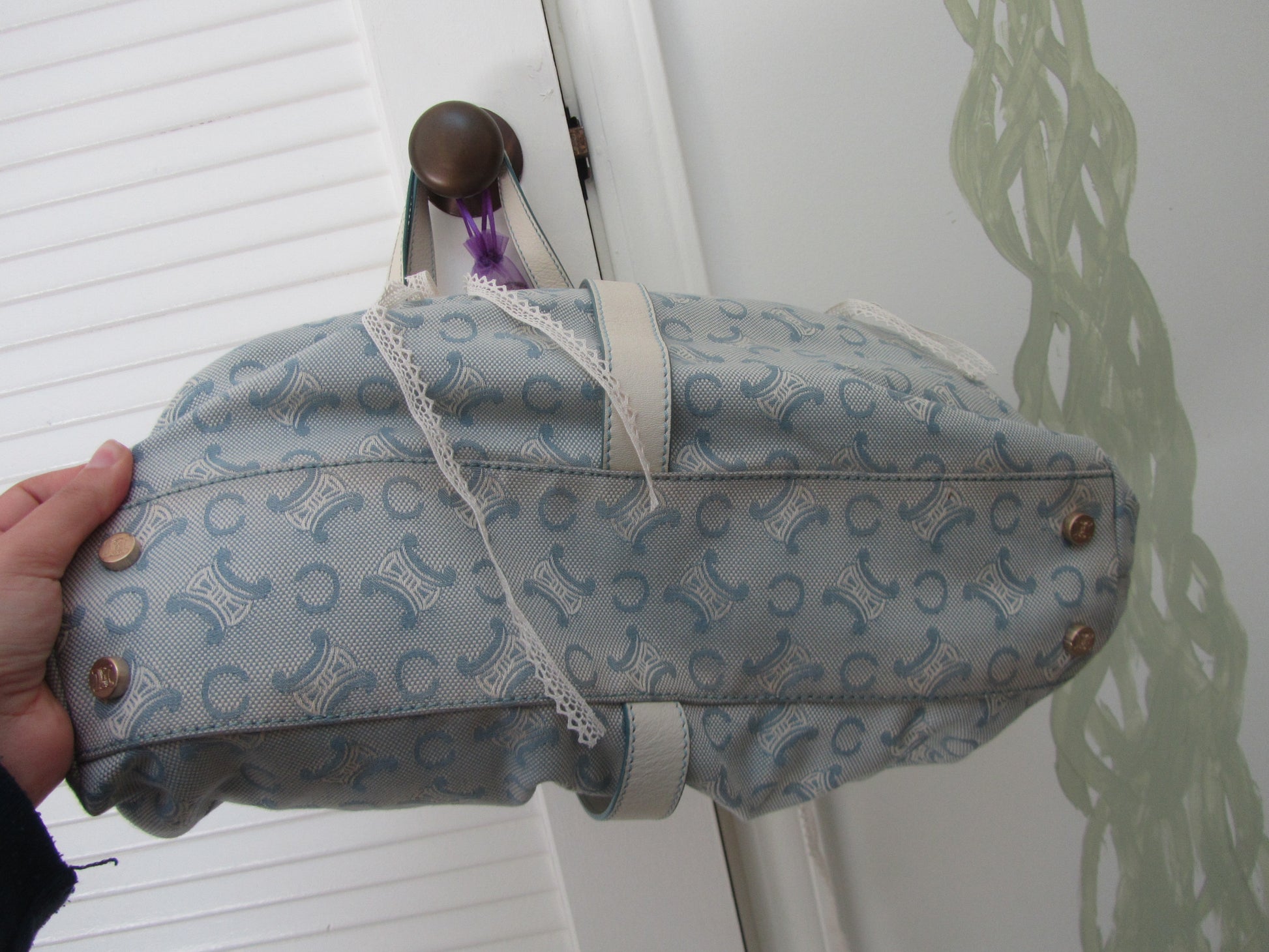 Patterned bag with decorative buttons held by a hand against a white background