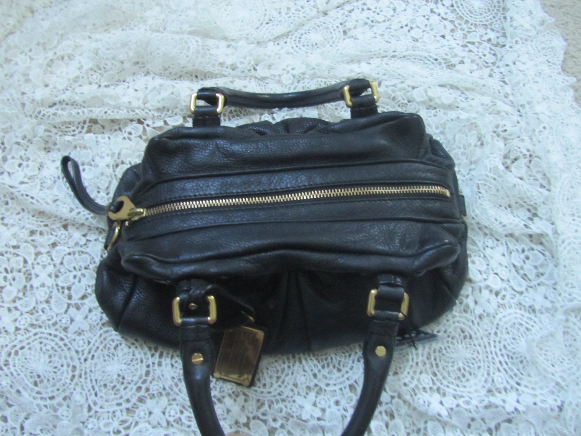 Black handbag with gold zippers on a textured white surface