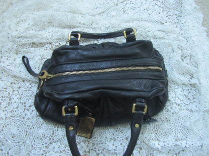 Black handbag with gold zippers on a textured white surface