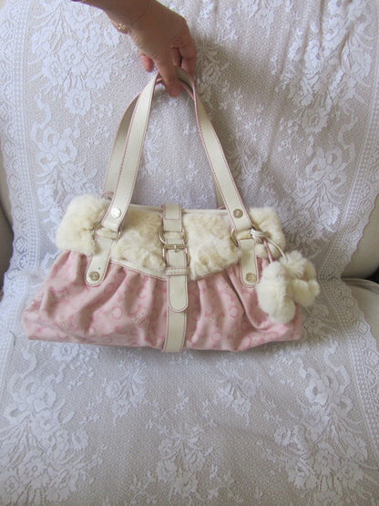 Pink handbag with white pom-poms on a textured white surface