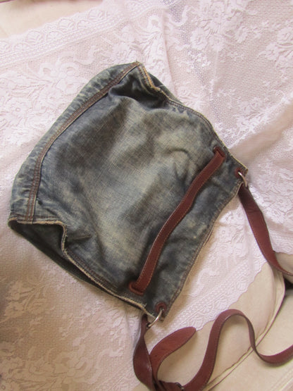 Denim handbag with a brown strap on a textured surface