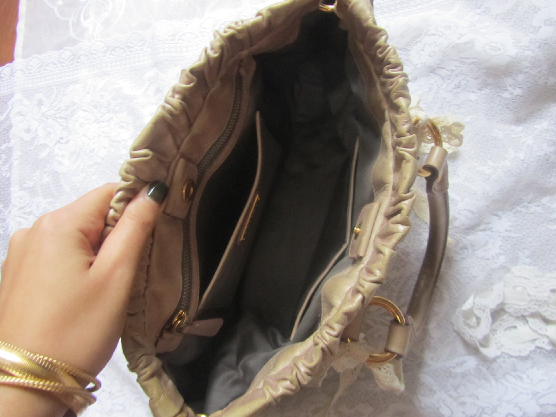 Beige handbag with ruffled details held by a hand on a white textured surface