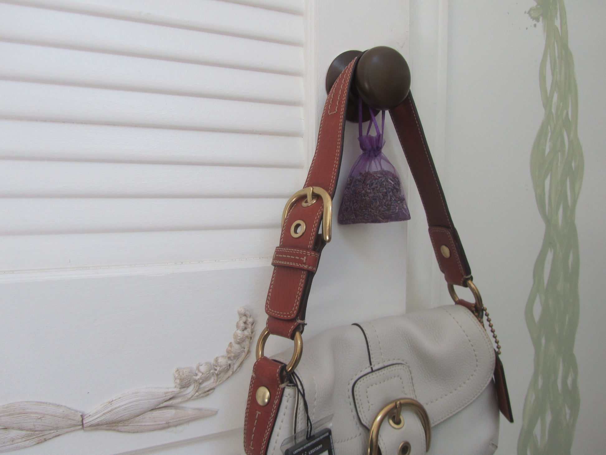 White handbag with brown strap hanging on a hook against a white wall.