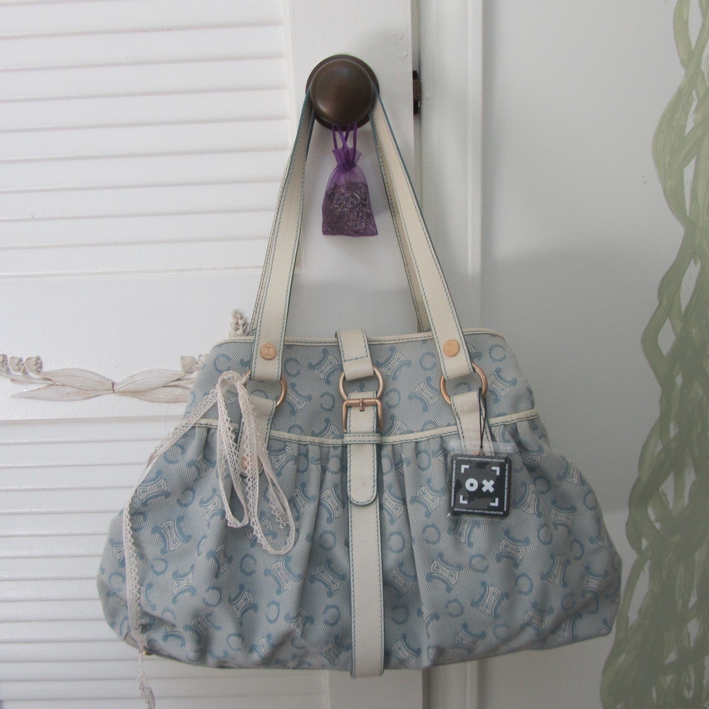 Blue patterned handbag with white handles hanging on a hook against a white wall.
