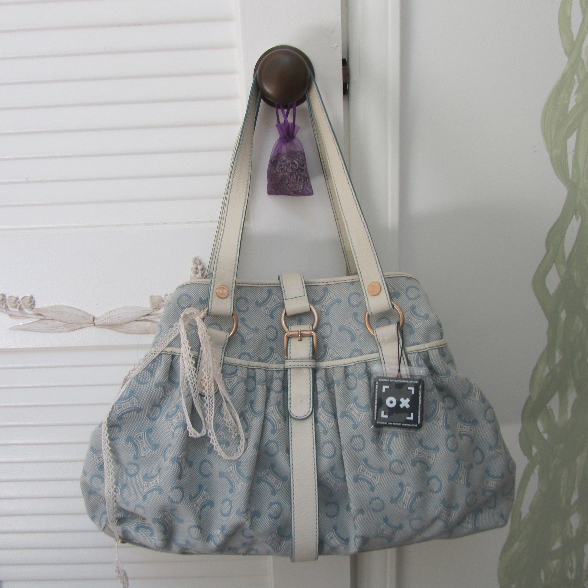 Blue patterned handbag with white handles hanging on a hook against a white wall.