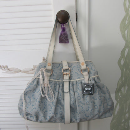 Blue patterned handbag with white handles hanging on a hook against a white wall.