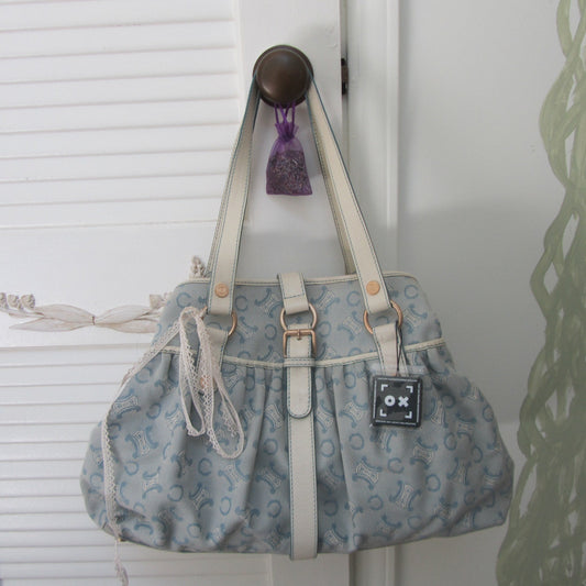 Blue patterned handbag with white handles hanging on a hook against a white wall.