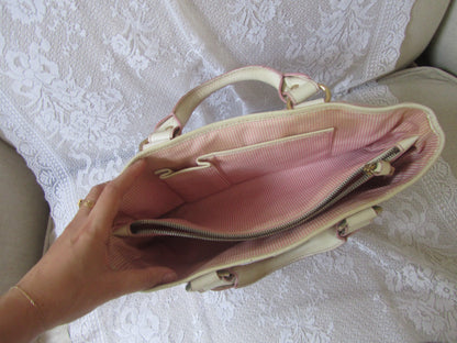 Beige handbag with pink interior held by a hand on a white lace background