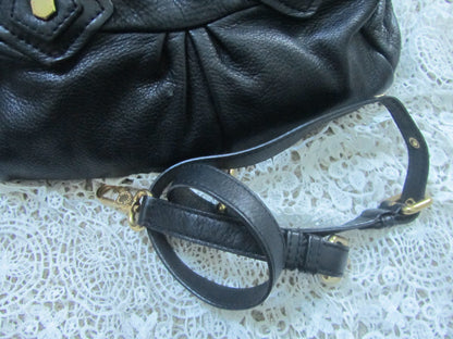 Black leather handbag with gold accents on a textured white surface