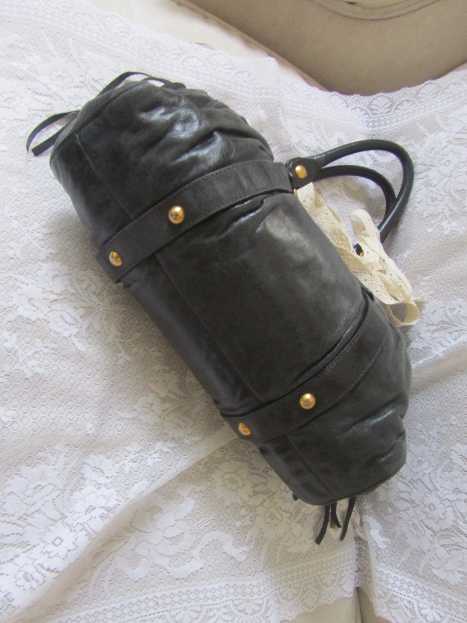 Black leather bag with gold studs on a textured white surface