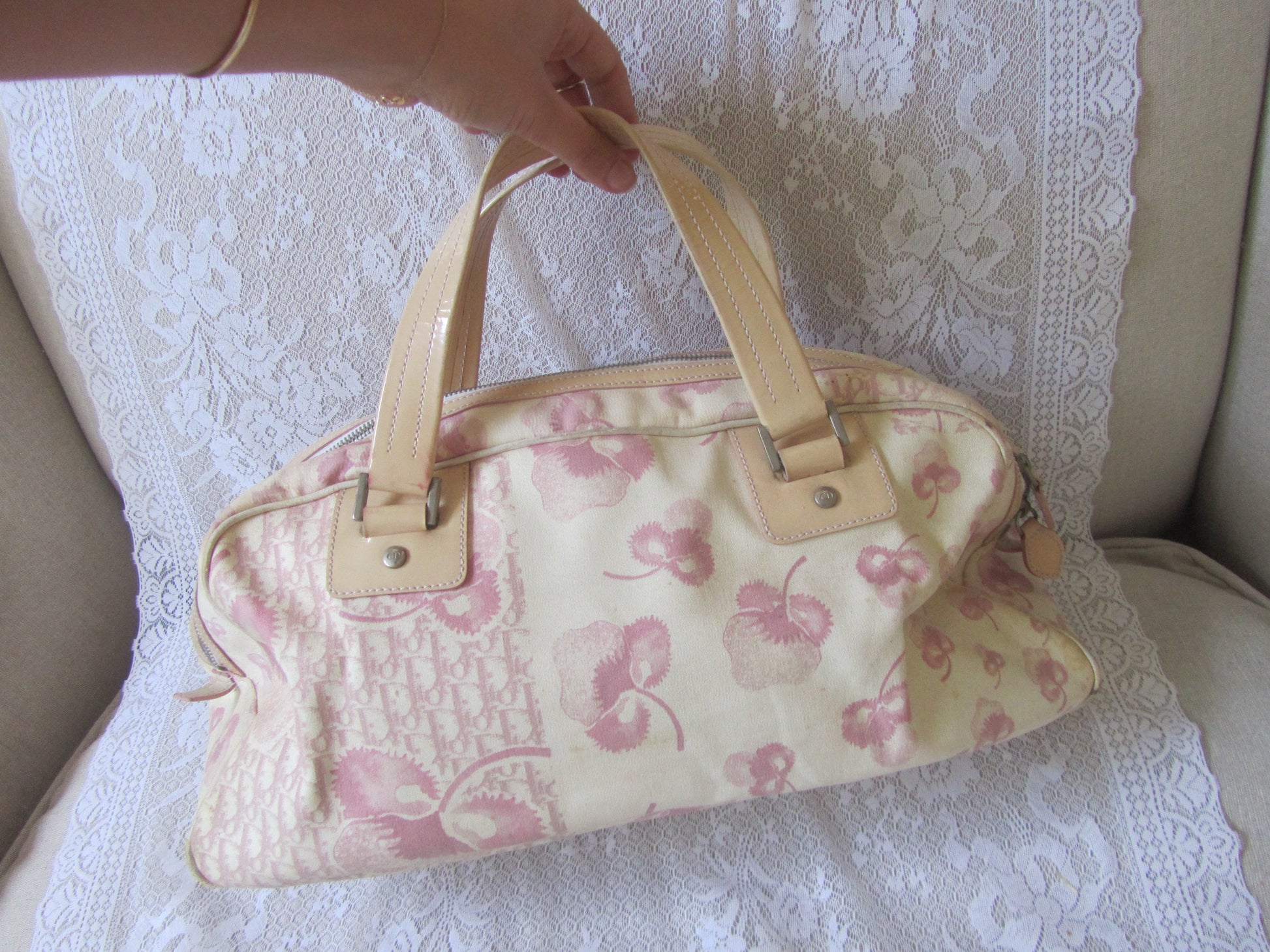 Floral patterned handbag held by a hand on a lace-covered surface