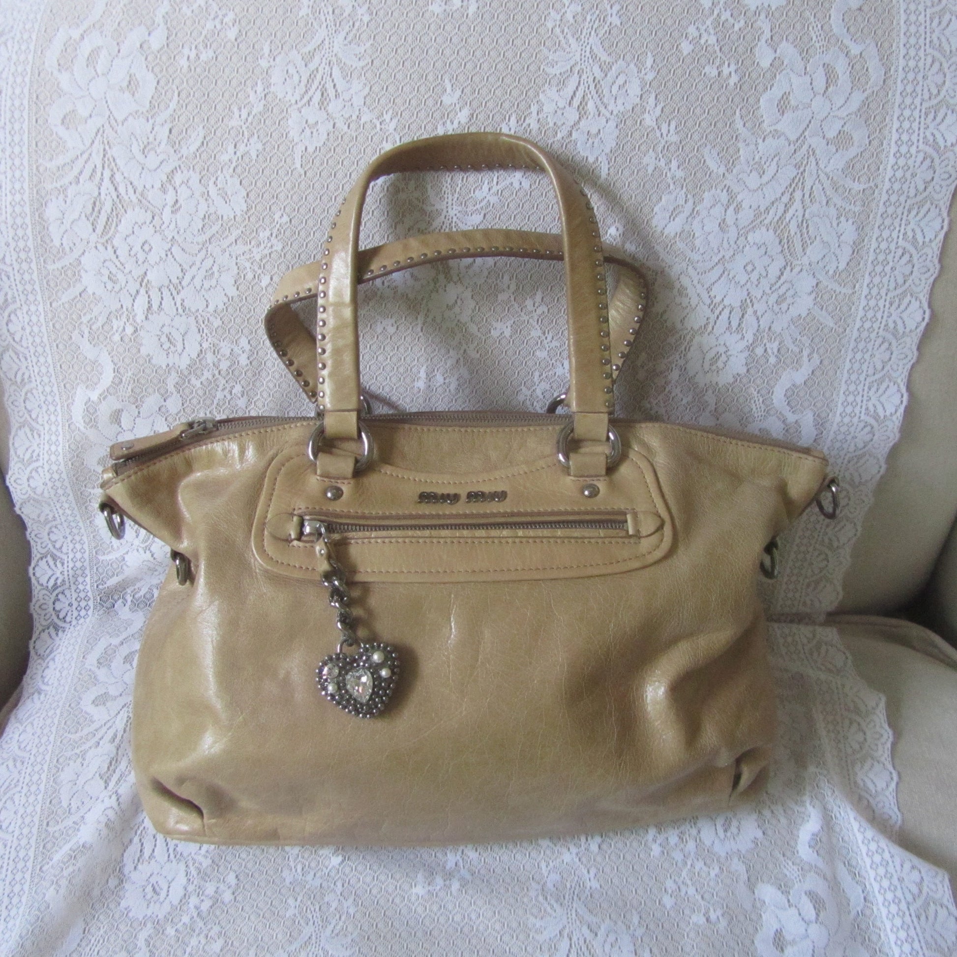 Beige handbag with decorative elements on a white lace fabric background