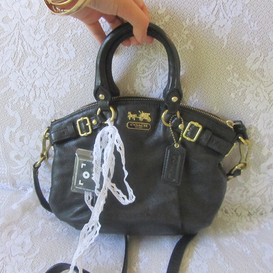 Black handbag with gold accents held by a hand on a textured white surface