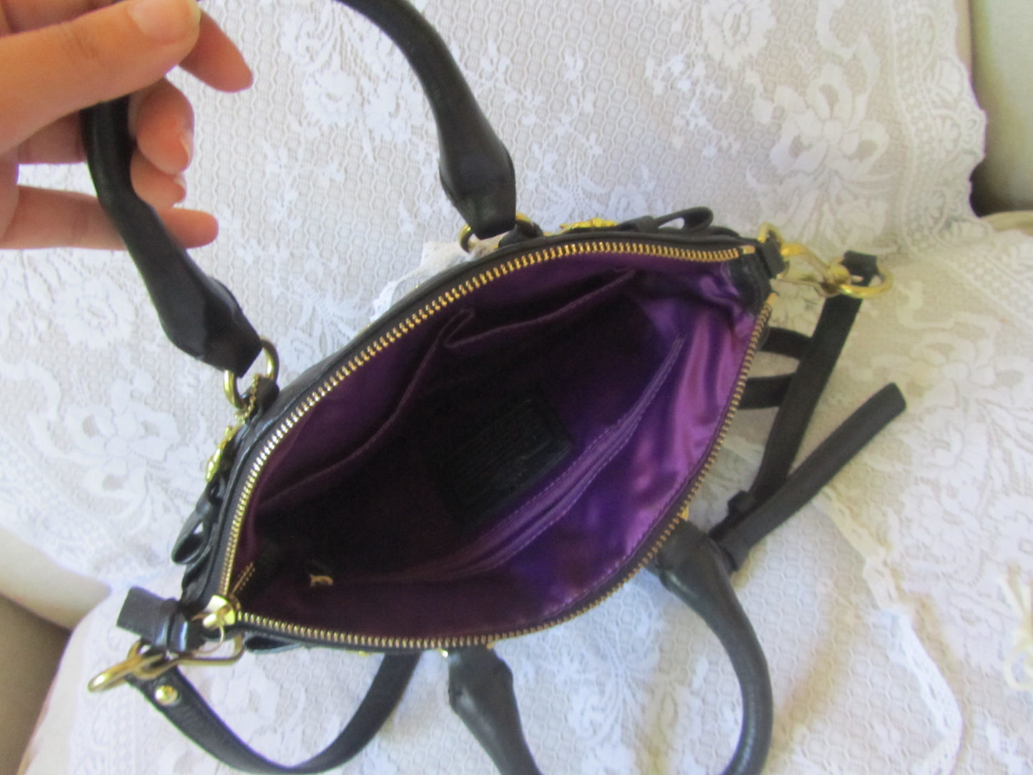 Black handbag with purple interior held by a hand on a textured white surface