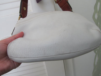 White leather handbag with brown strap held by a hand against a white background