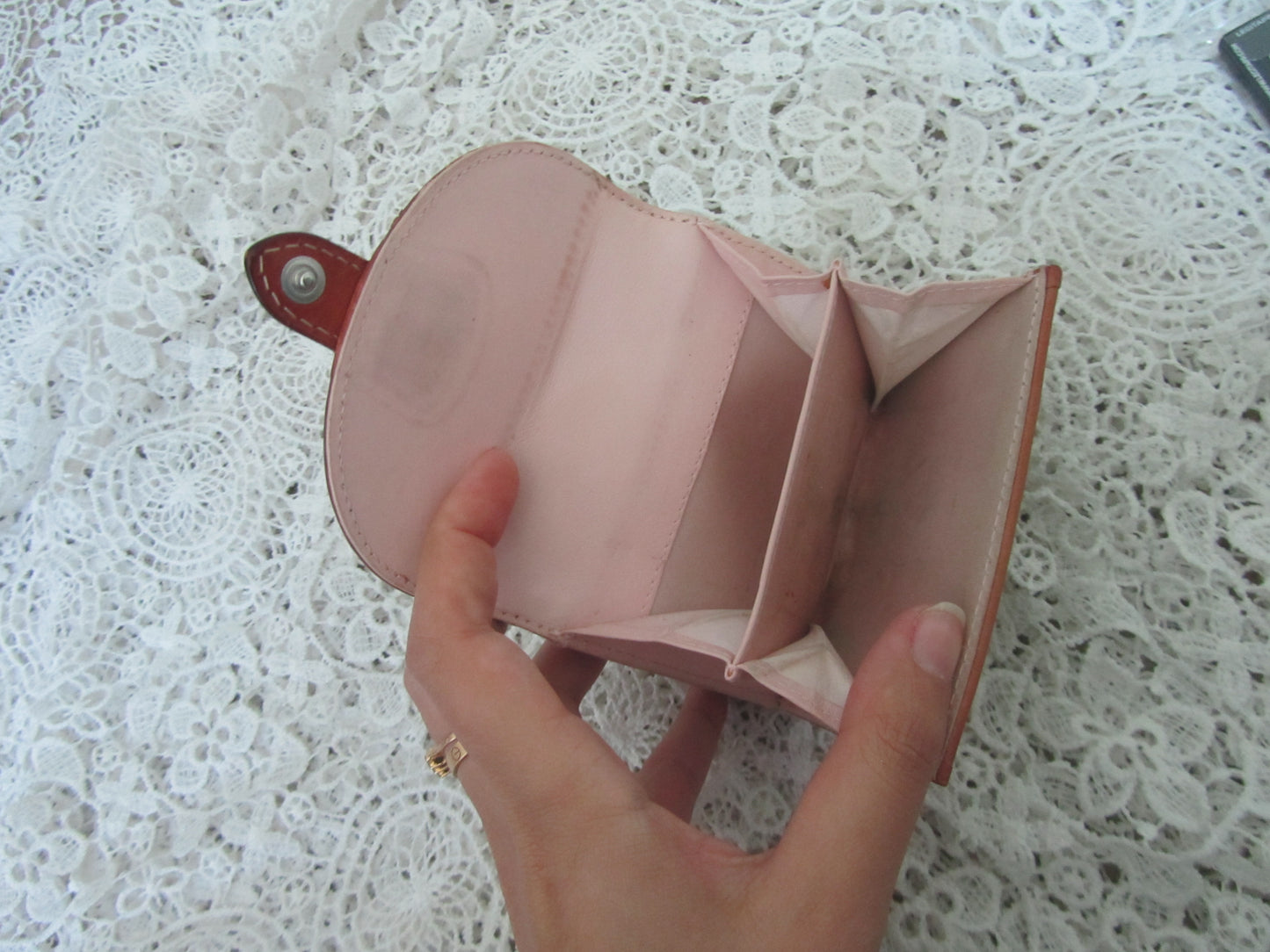 Pink leather wallet held by a hand on a textured white surface
