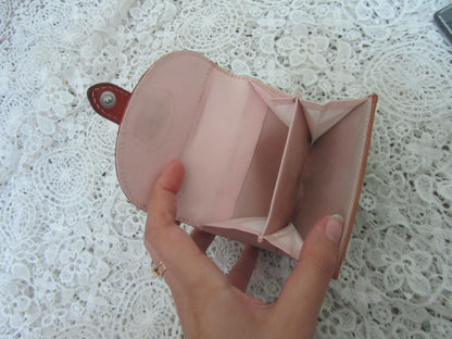 Pink leather wallet held by a hand on a textured white surface