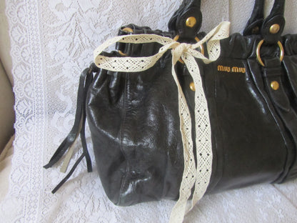 Black leather handbag with a lace ribbon on a textured white surface