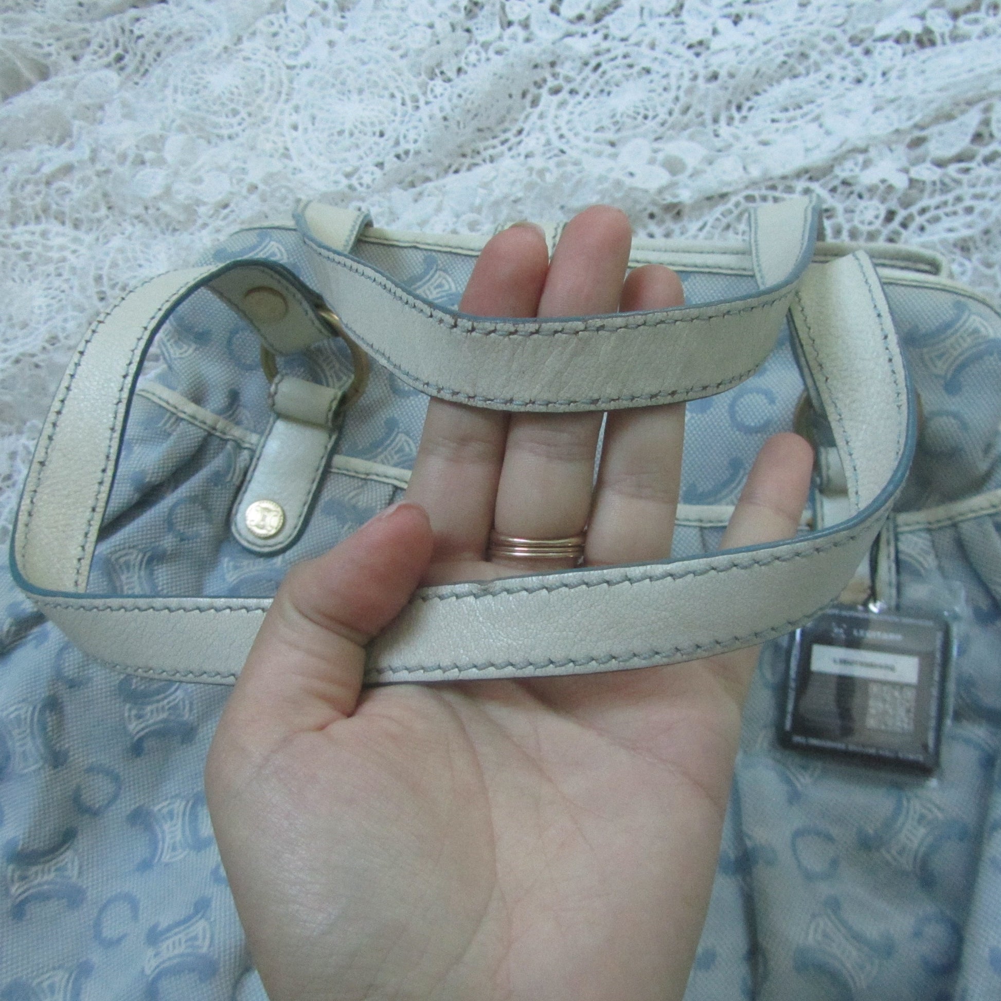 Hand holding a beige leather strap on a lace surface