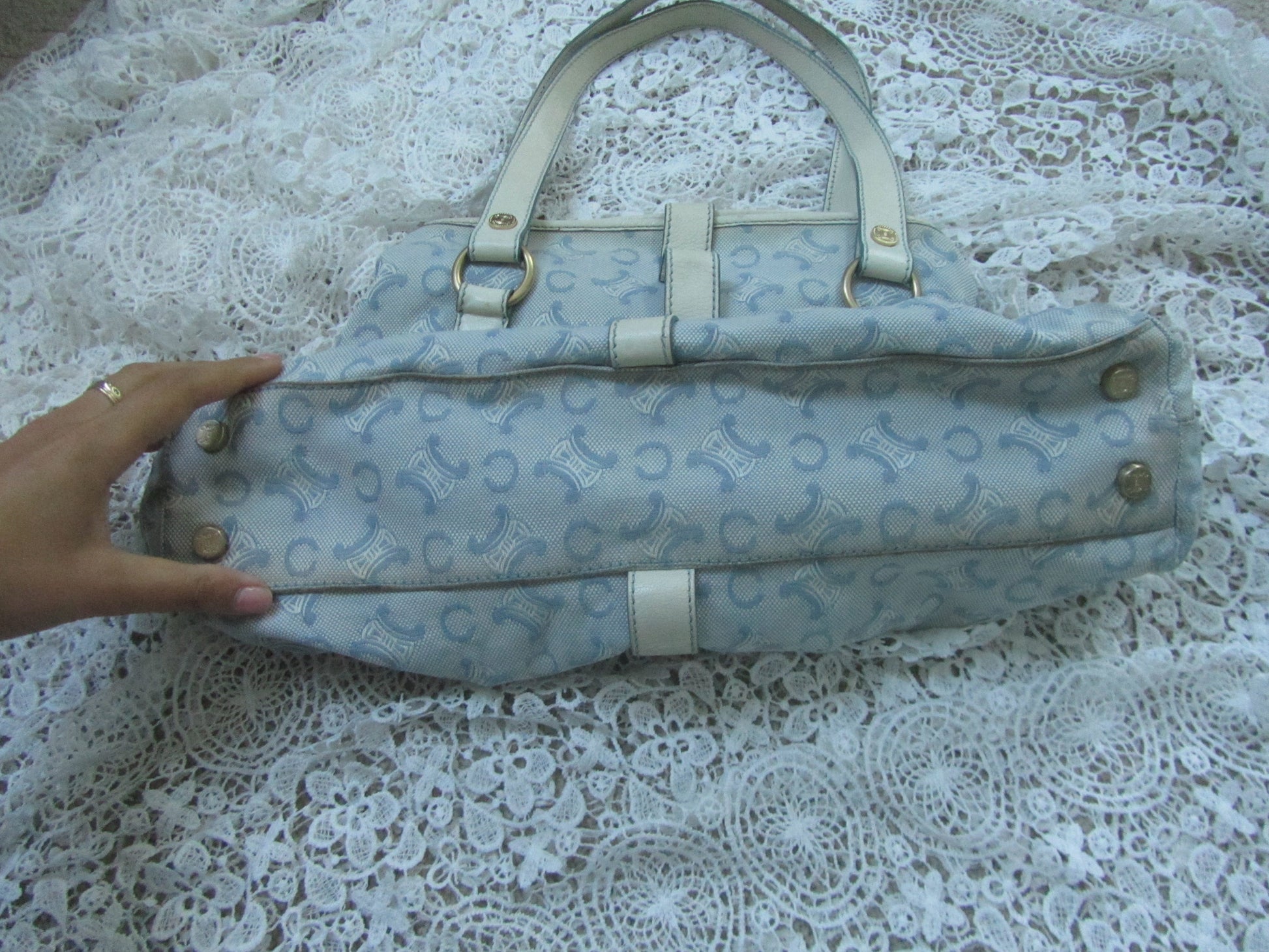 Light blue patterned handbag held by a hand on a lace tablecloth