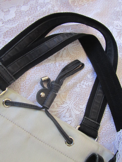 Close-up of a black strap attached to a beige bag on a textured white background